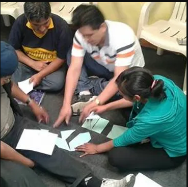 A group of people sitting on the floor looking at papers.